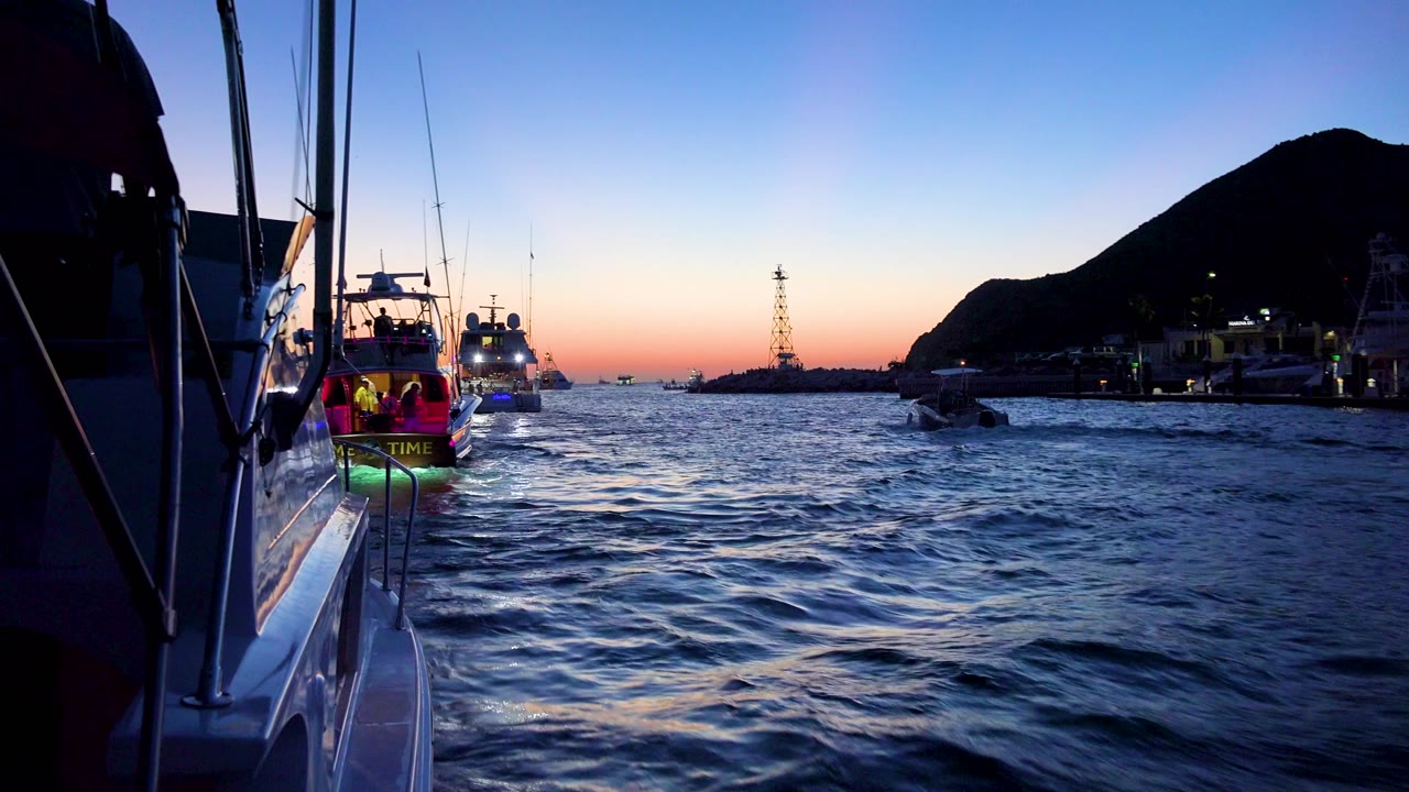Cabo San Lucas boat traffic fills the midground, including a stern with green light near the left side, choppy water, a horizon tower, and a dark shoreline, no visible people.