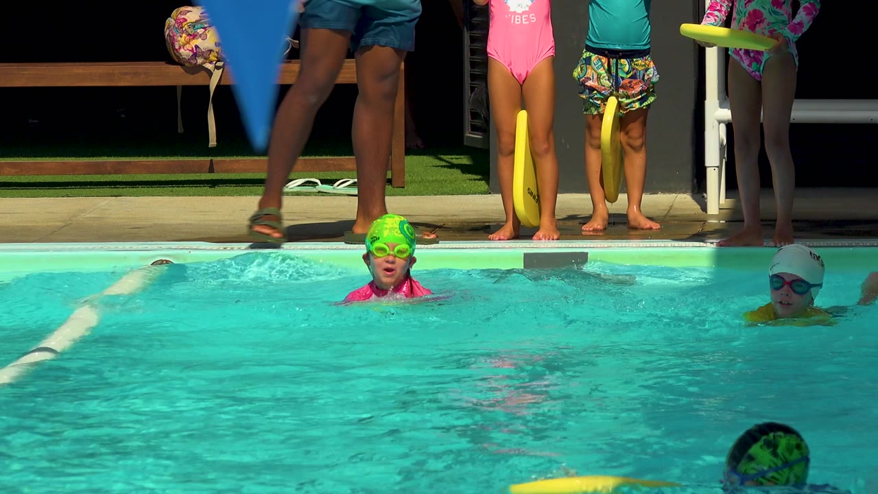 Child in green swim cap faces camera in a pool lane.