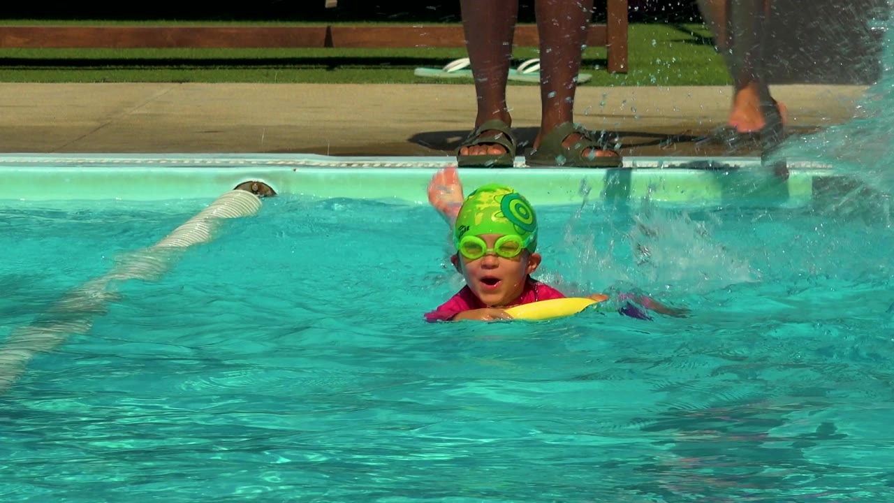 Young boy in green swim cap near splashing pool water.