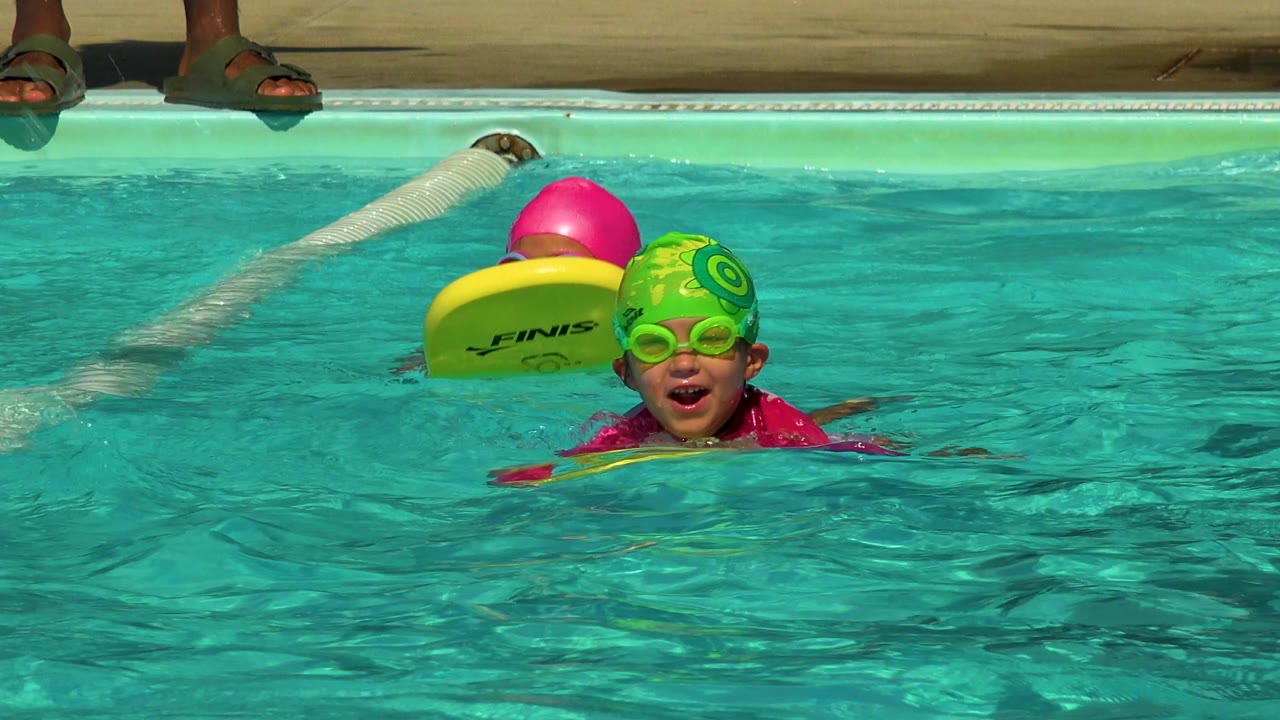 Smiling child in green swim cap near a yellow kickboard.