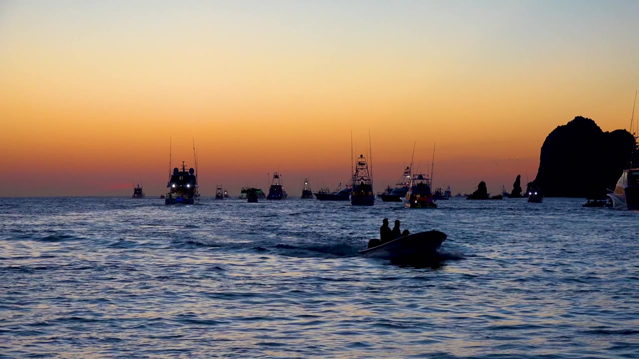 Boat silhouette lower right with distant vessels and rock formation at dusk.