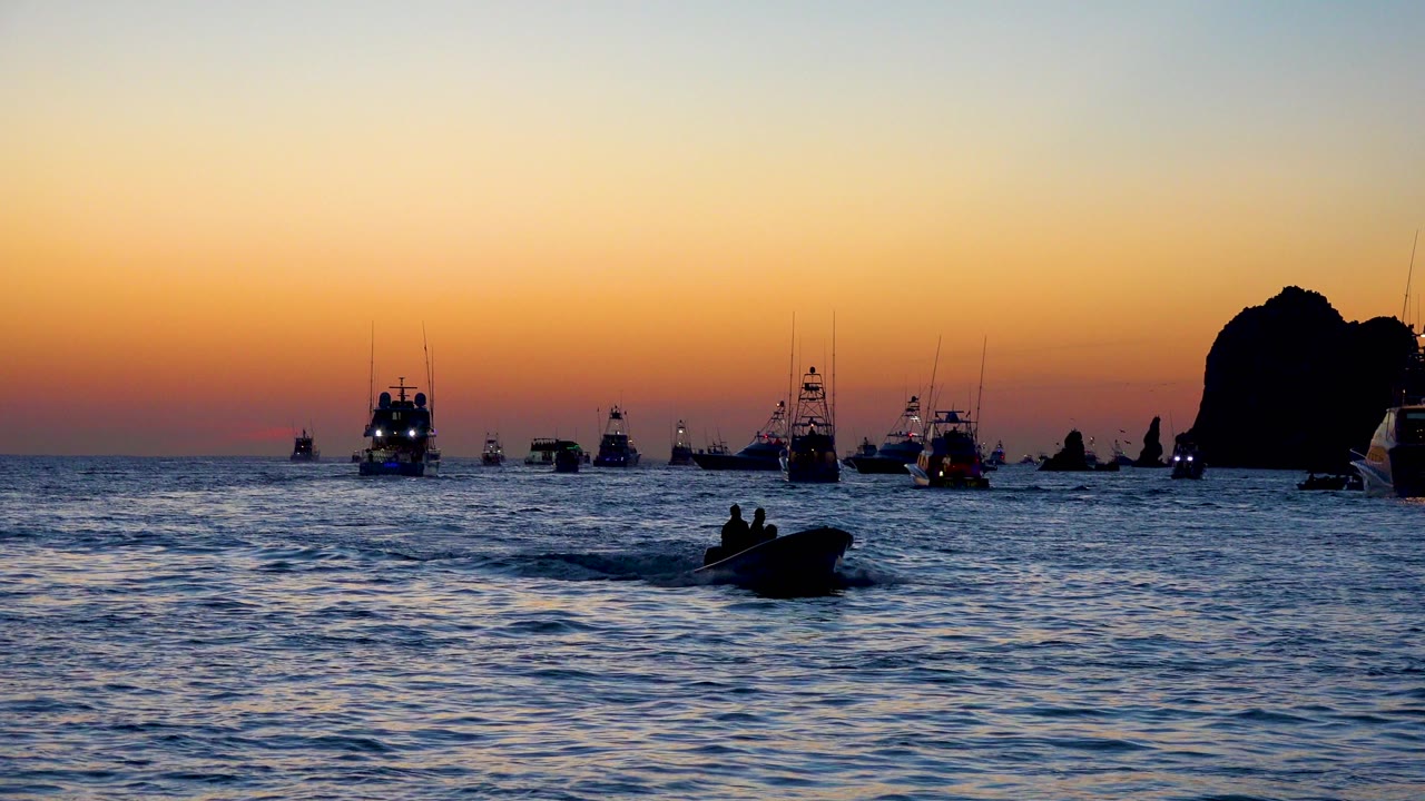 Boats on the horizon at sunset with a low motorboat crossing the water.