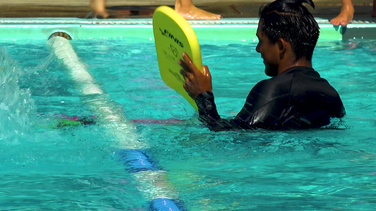Man raises a yellow kickboard while standing in the pool.