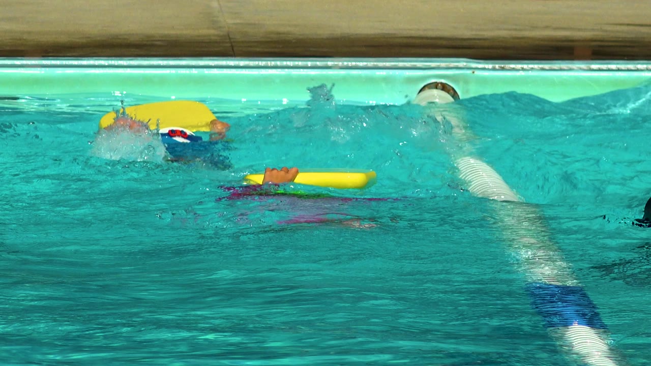 Children in a Cabo San Lucas pool move through lane water with yellow kickboards and splashes near the top of the frame.