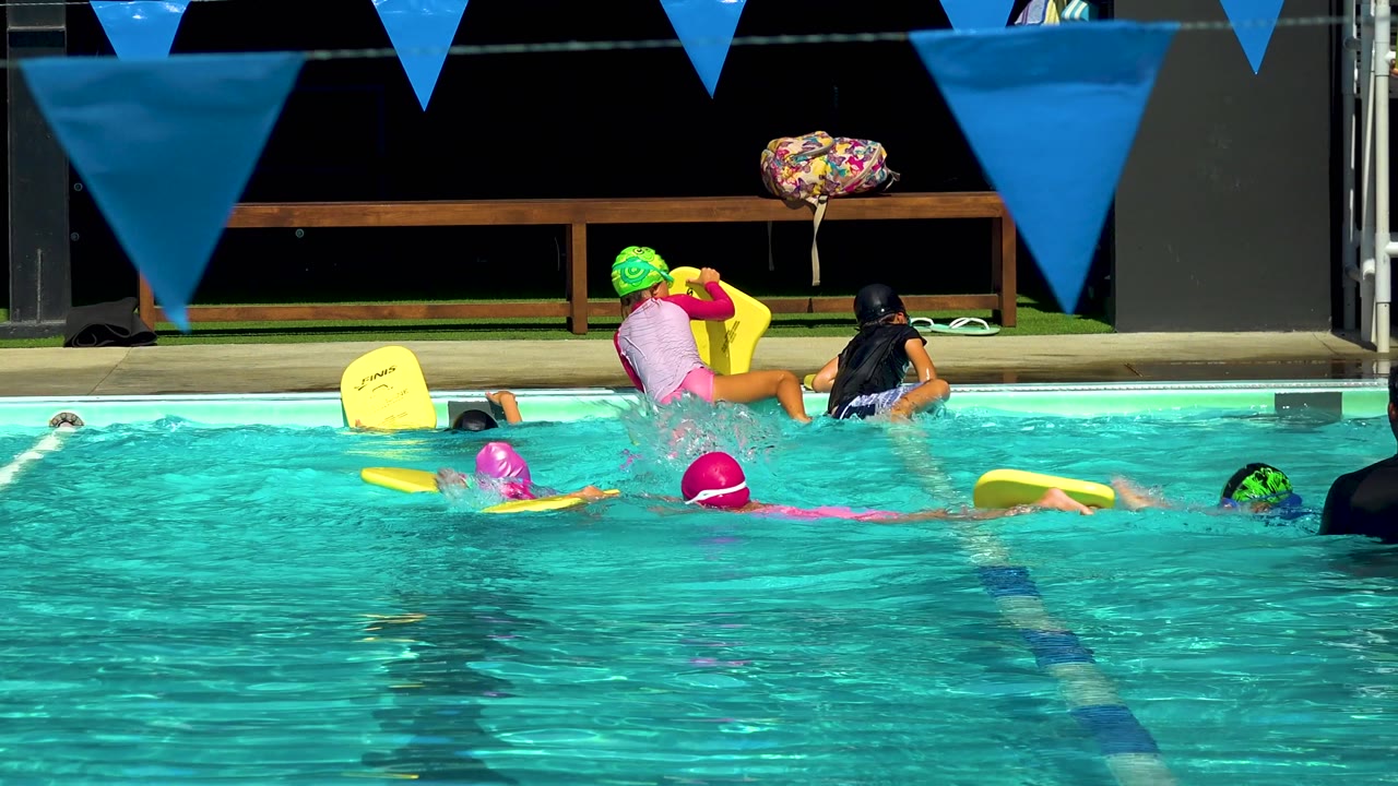 Swimmers with colorful caps continue across the pool.