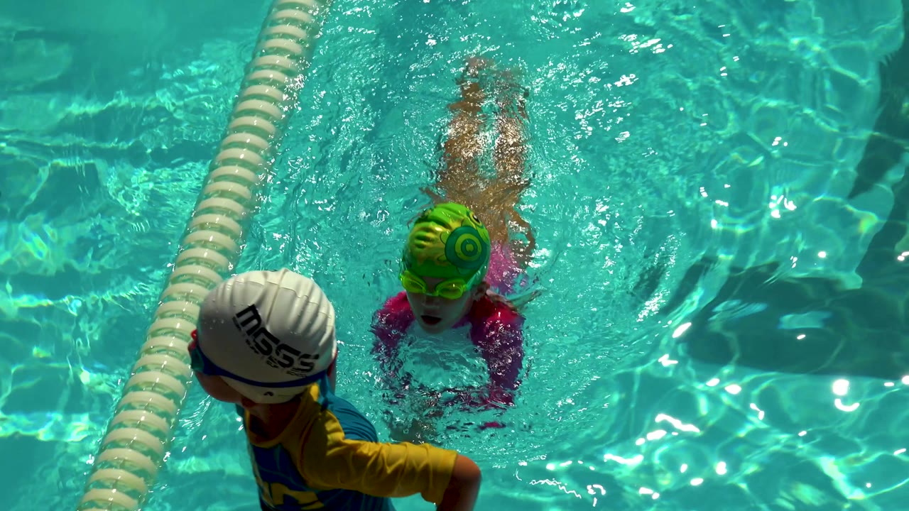 Girl in green swim cap swimming beside a lane divider.