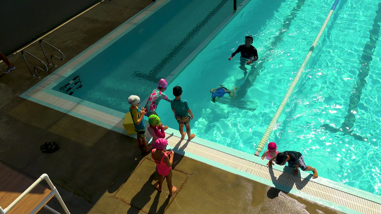 Children watch from the deck as an instructor stands in the pool.