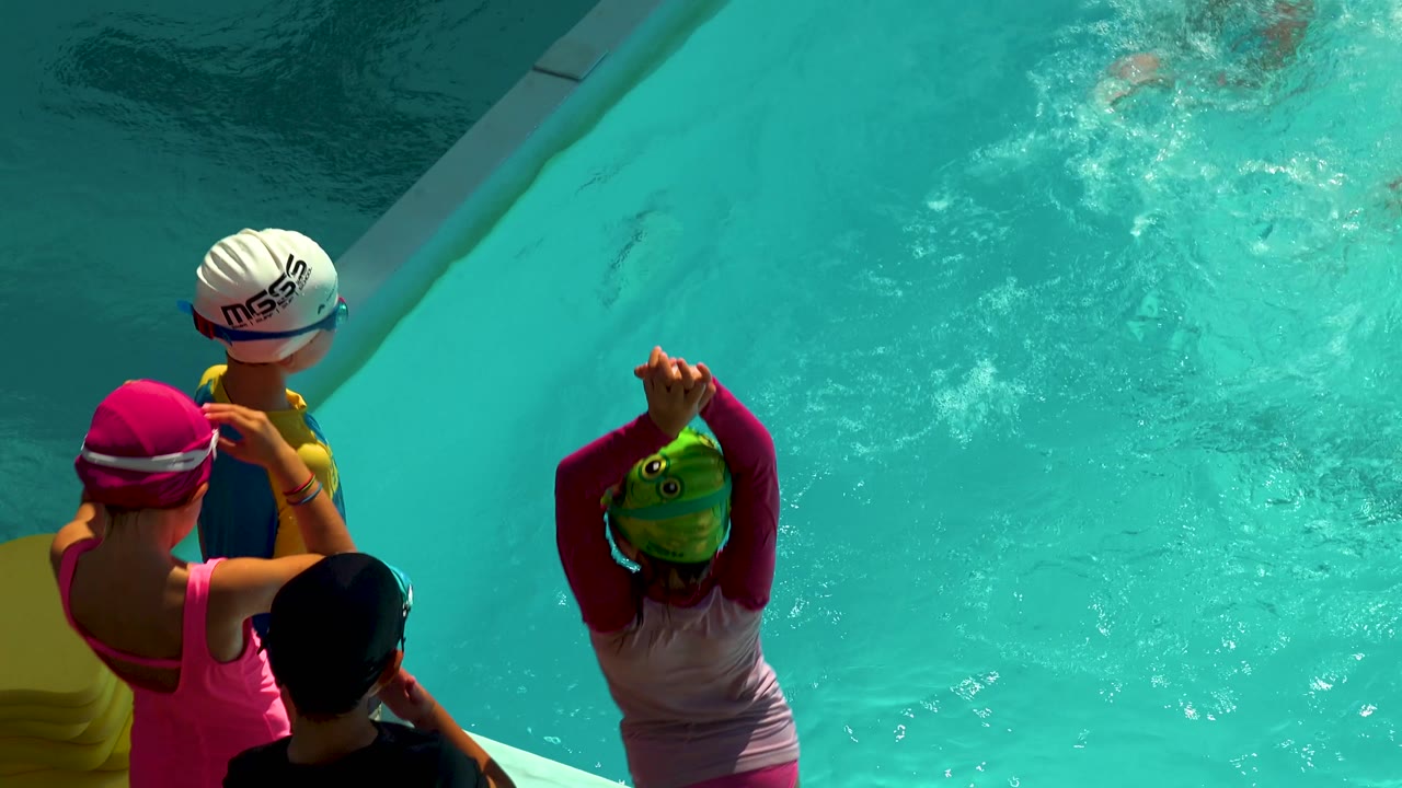 Young swimmers adjust goggles beside turquoise pool water.