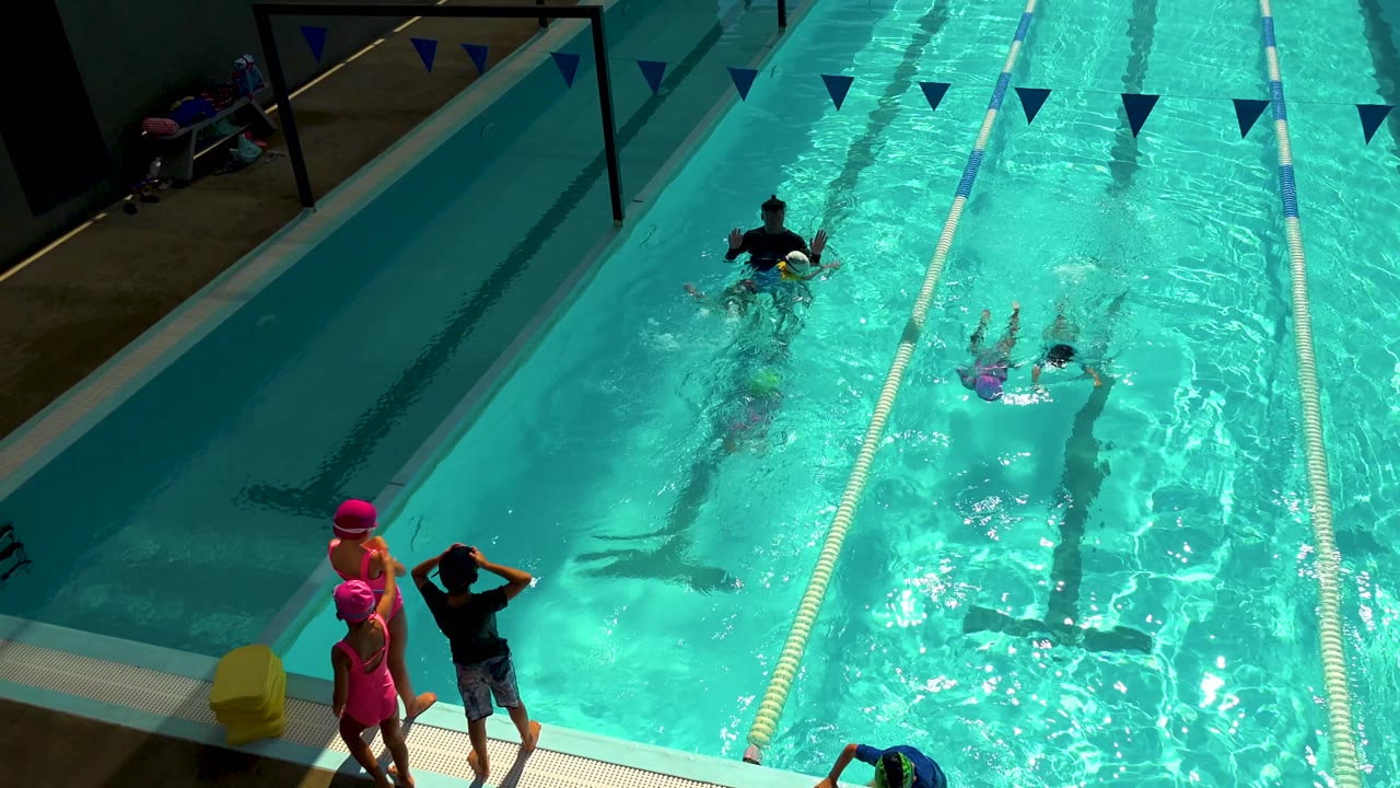 Coach and children continue swim drills in marked pool lanes.