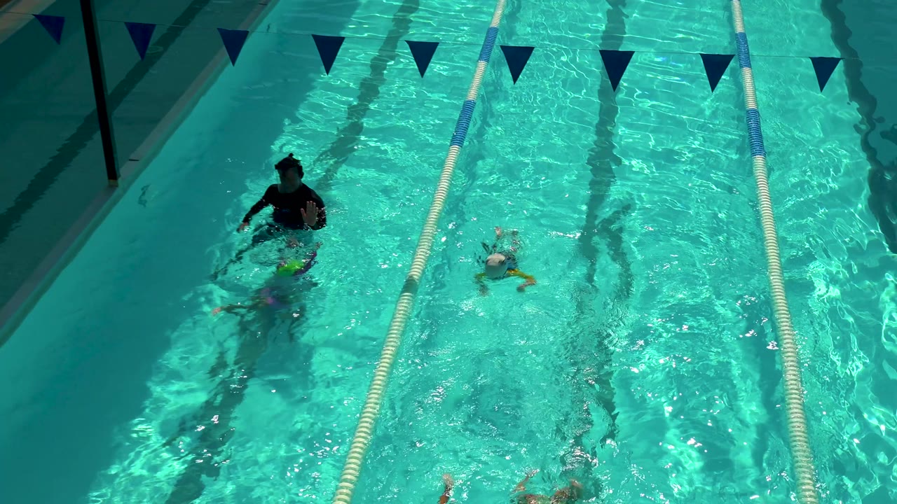Children swim near an adult in adjacent pool lanes.