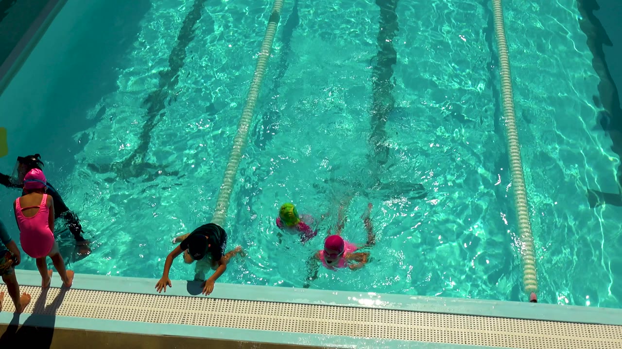 Children swimming near a pool edge with adults standing nearby.