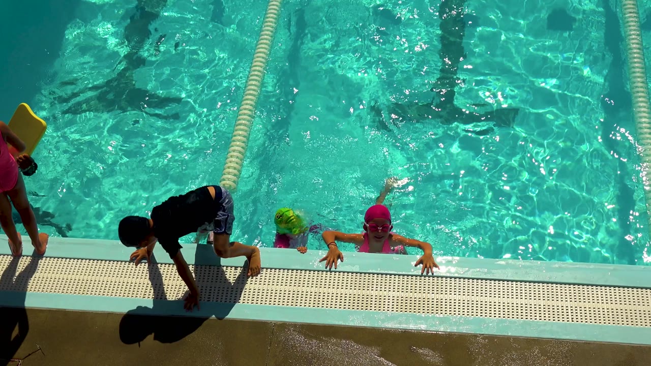 Children hold the pool edge as another child steps onto the deck.