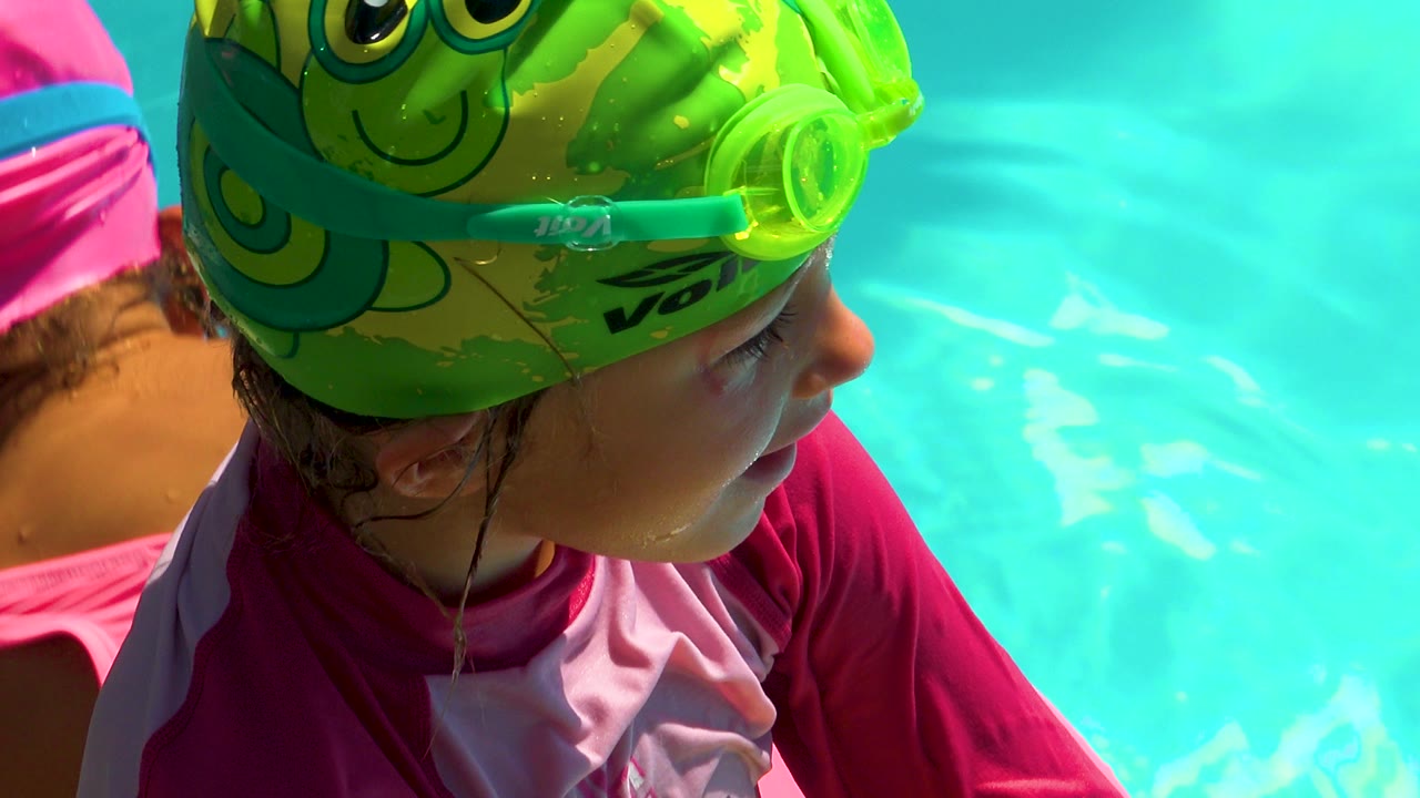 Child in pink swim shirt looking across the swimming pool.