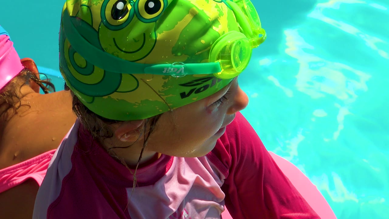 A closer moment shows the child in Cabo San Lucas angled toward the right side of frame, with her green swim cap and goggles filling the upper foreground against rippled pool water.