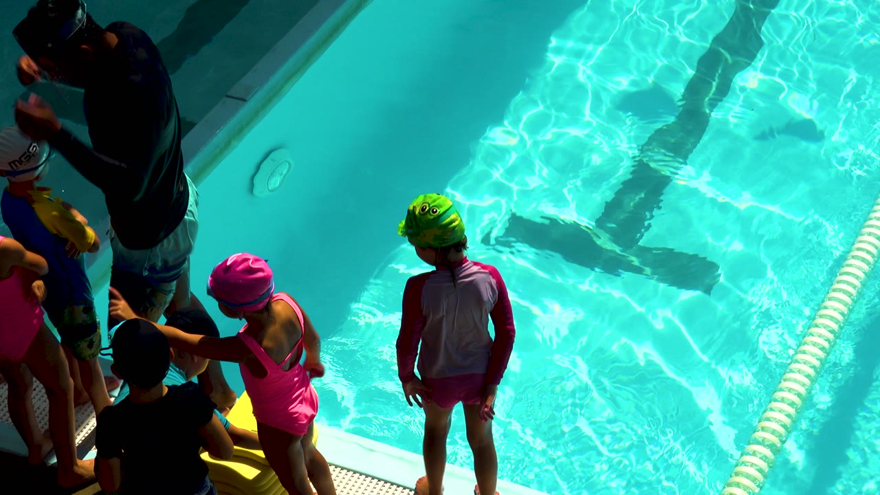 Children wait near the pool edge as sunlight reflects on the water.