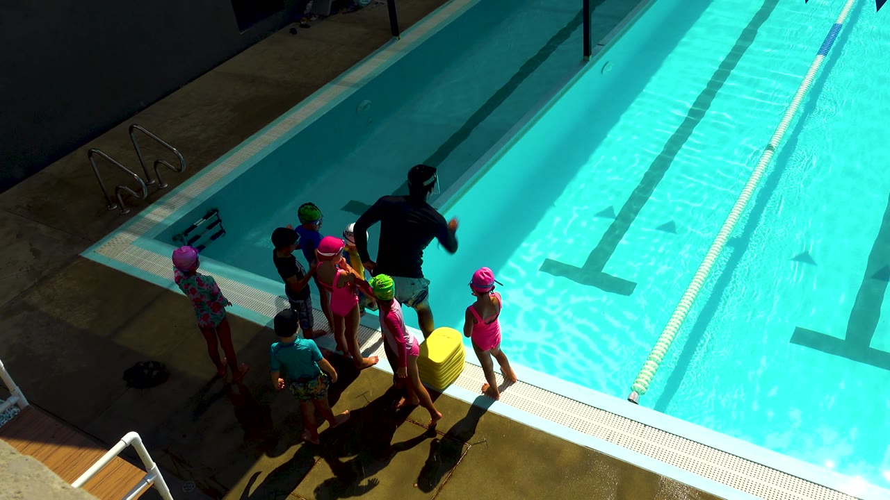 Adult and children gathered on the pool deck beside lap lanes.