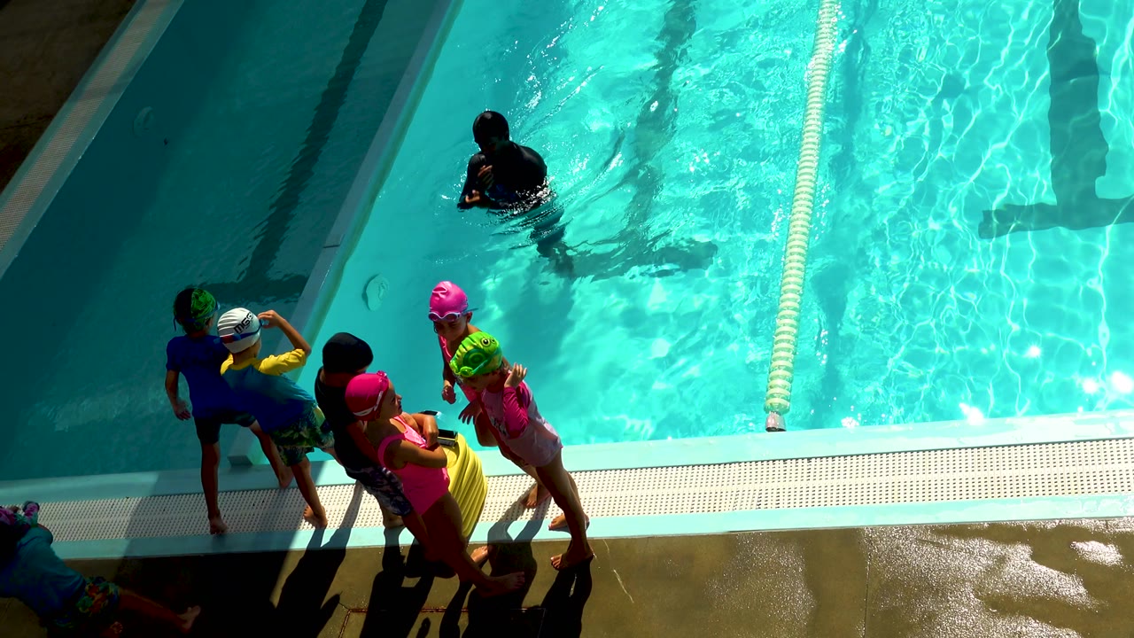 Children wait at the pool edge while a person remains in the water nearby.