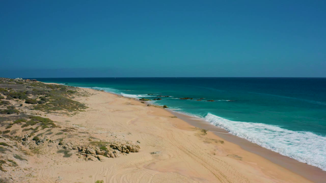 Wide beach shoreline with scrubland and blue sea