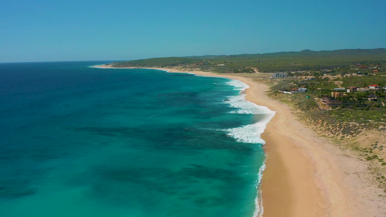 Aerial coastline with white waves breaking onto empty sand.
