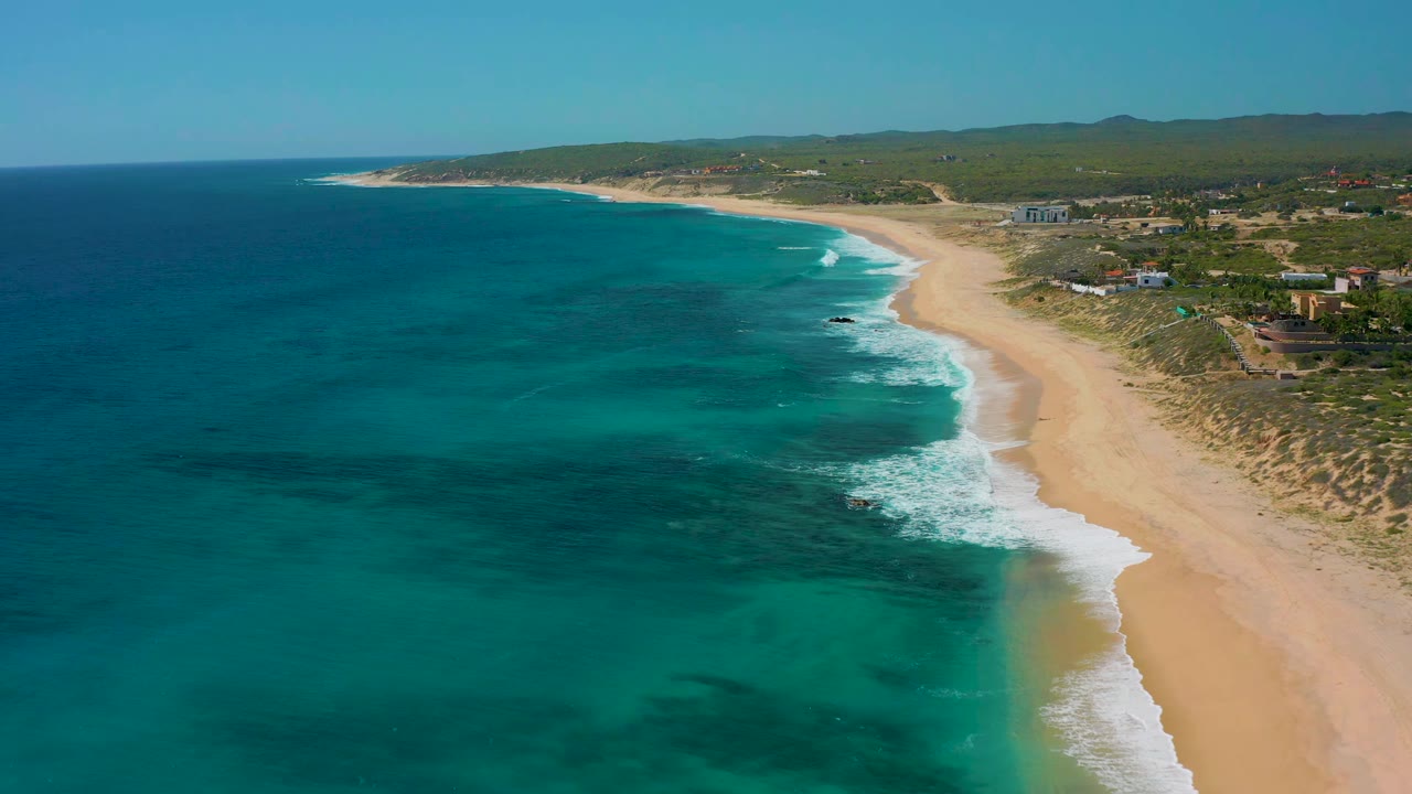 Curving sandy shoreline with mild surf and clear blue water.
