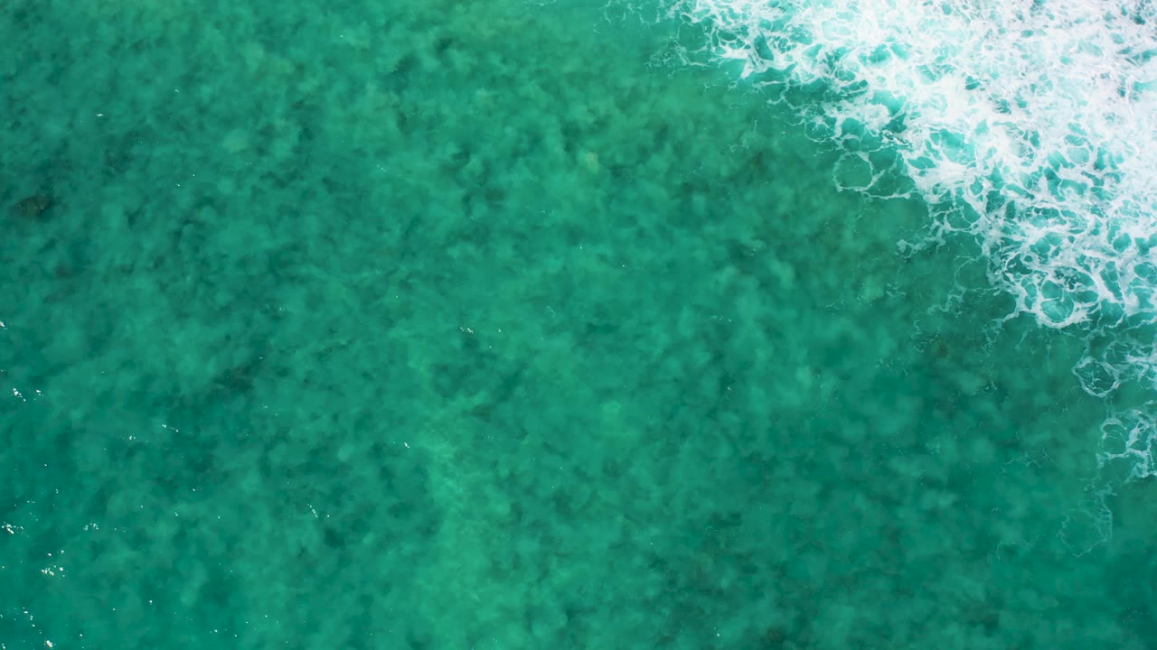 Overhead El Cardoncito sea surface with a brighter white foam band across the upper frame and mottled darker water below, no visible people.