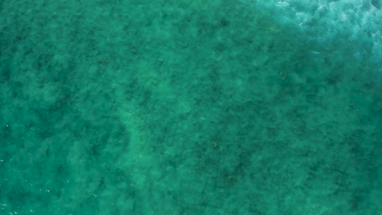 Teal shallow sea at El Cardoncito seen from above, with scattered small white highlights on the surface and no visible people.