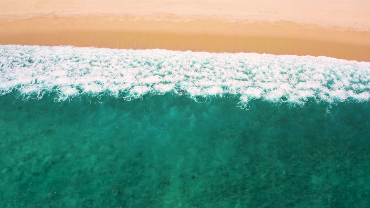Overhead view of El Cardoncito surf forming a bright white band between pale sand and turquoise-green water, with no visible people.
