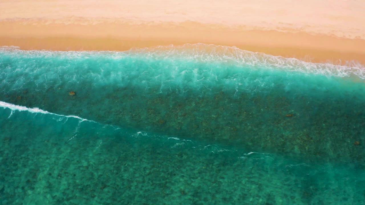 Overhead turquoise surf beside pale sand.