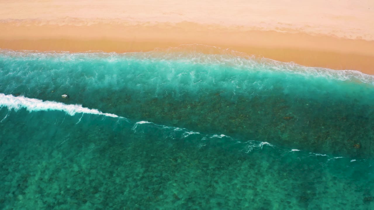 Overhead El Cardoncito shoreline view with a brighter white surf streak crossing the turquoise shallows below the sand, with no visible people.