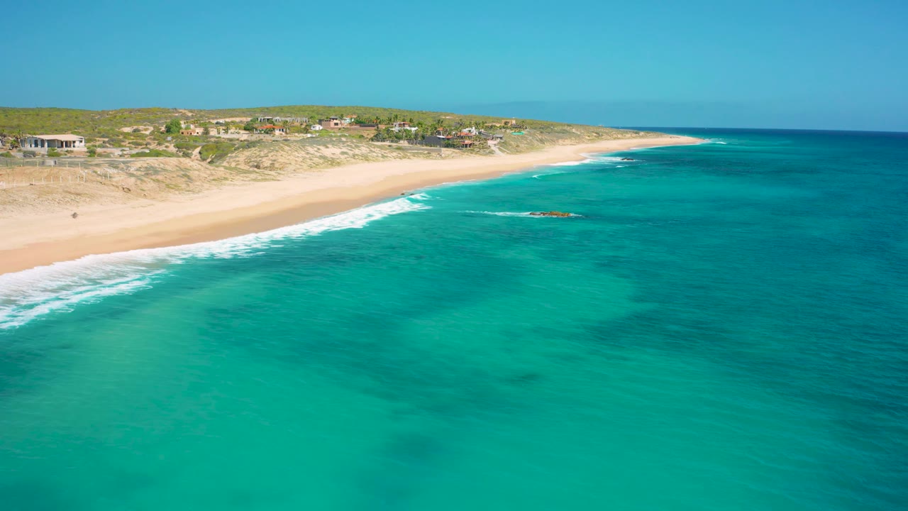 Aerial beach view with turquoise water, white surf, dunes, and coastal homes.