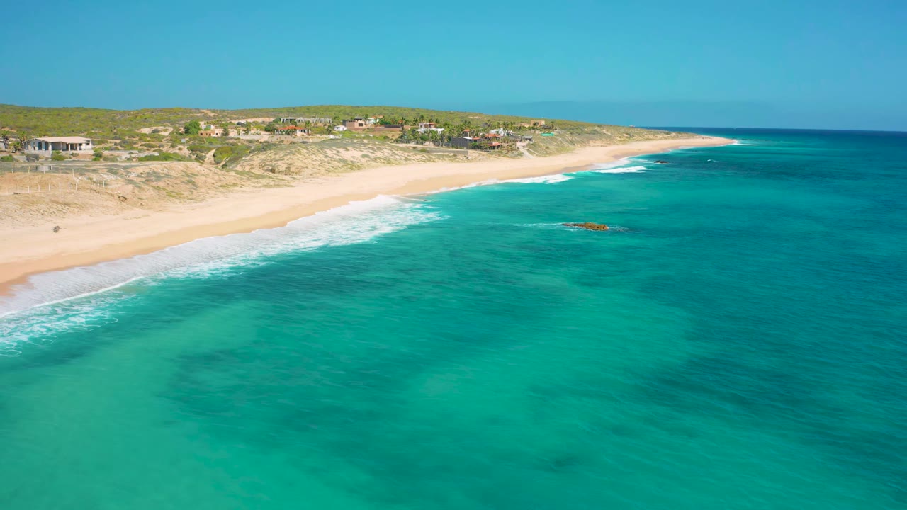 Wide aerial shoreline with blue water, sand, dunes, and coastal buildings