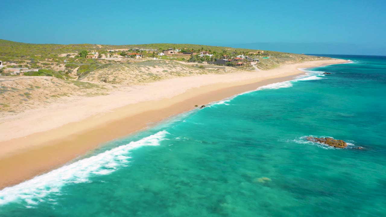 Wide aerial shoreline with surf on the left and clear water on the right.