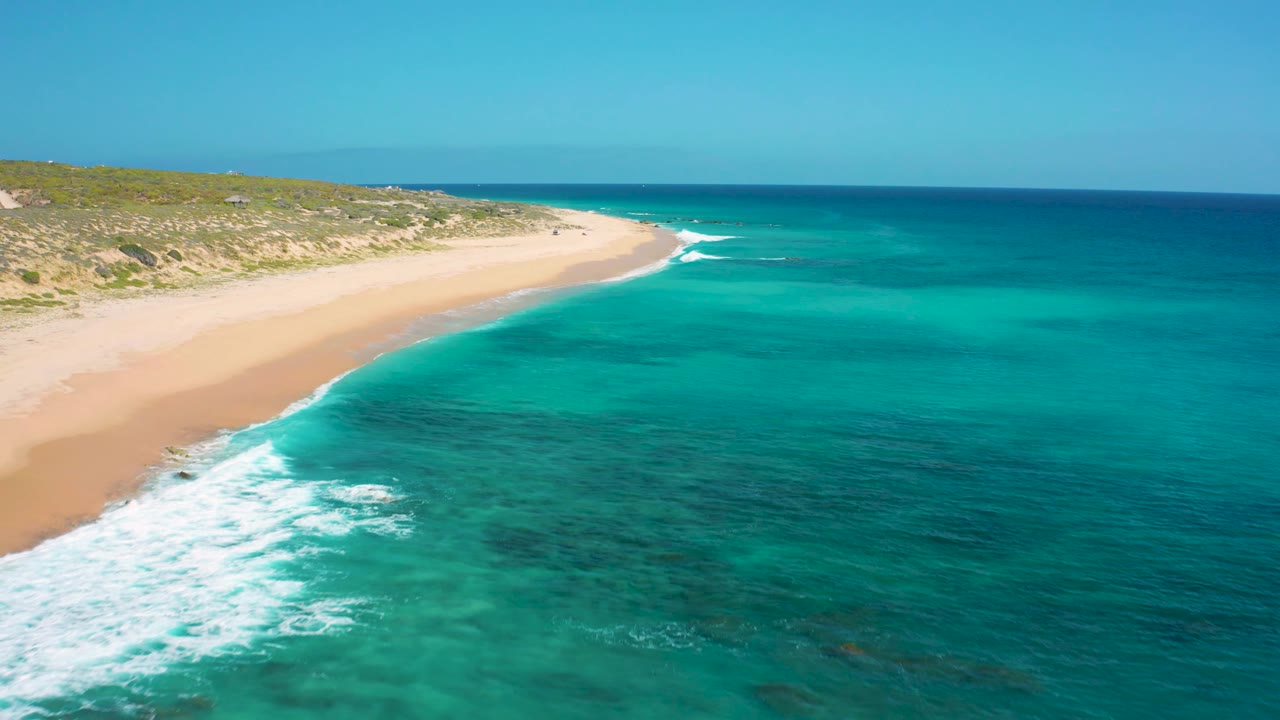Aerial frame at El Cardoncito with whitewater entering from the lower left, sandy beach running toward the center, teal ocean on the right, and no visible people.