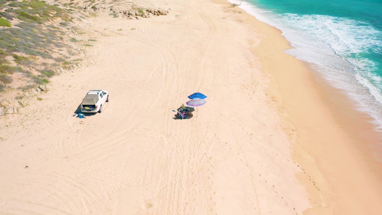 White car and umbrella setup viewed from above near the shoreline.