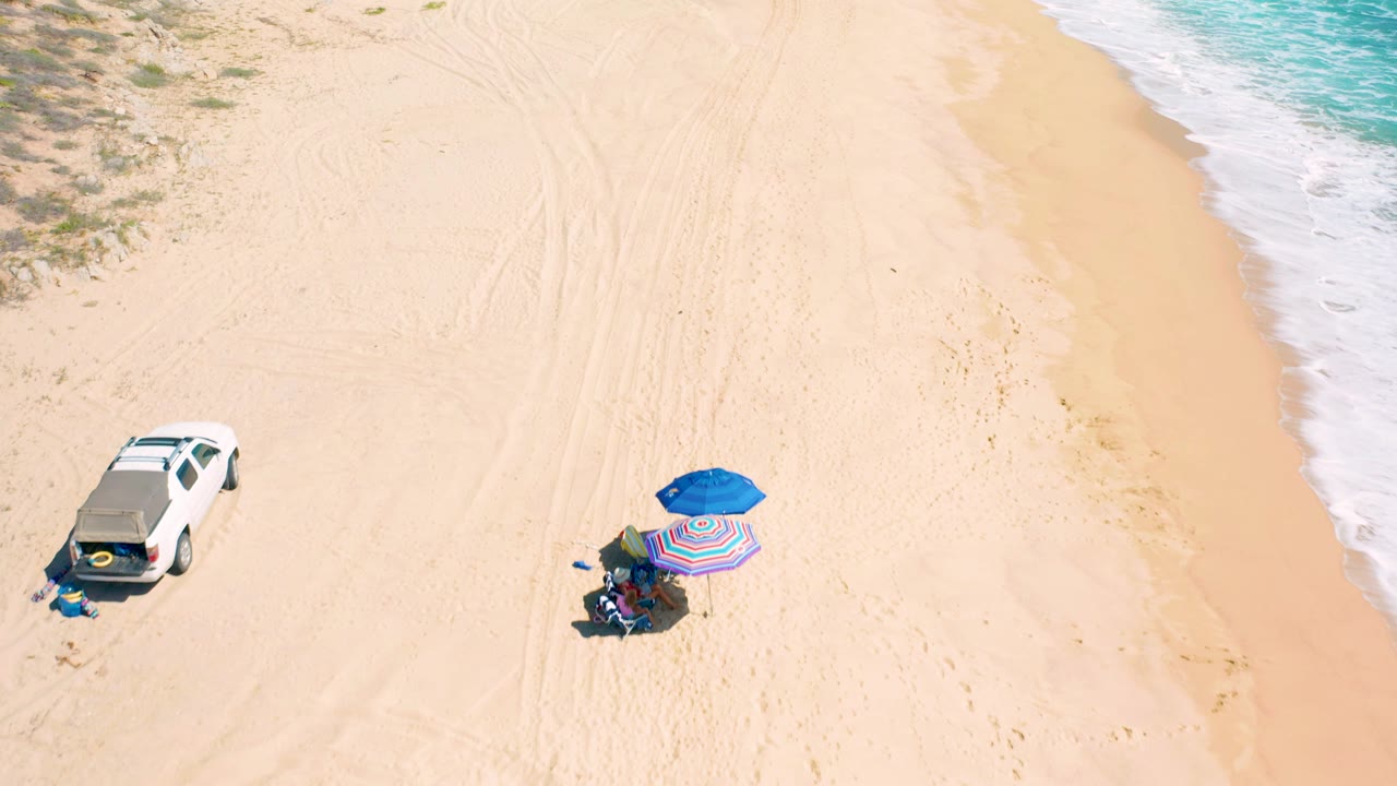 Aerial view of white SUV, umbrellas, sand, and surf.