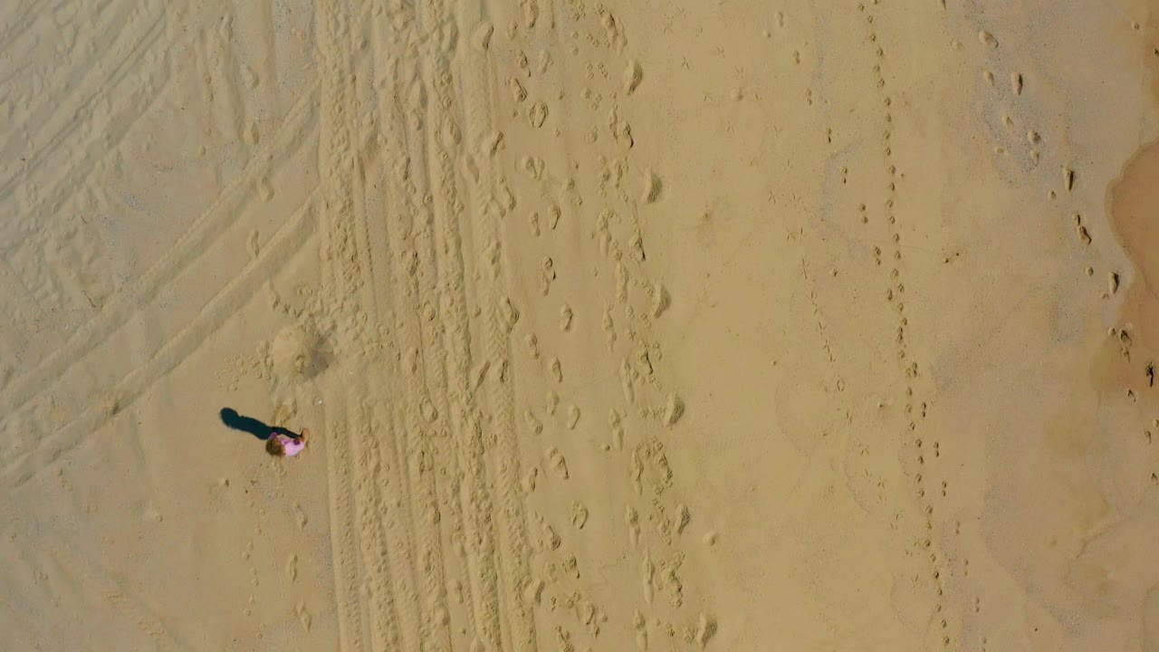 Small person walking across sand with footprints nearby.