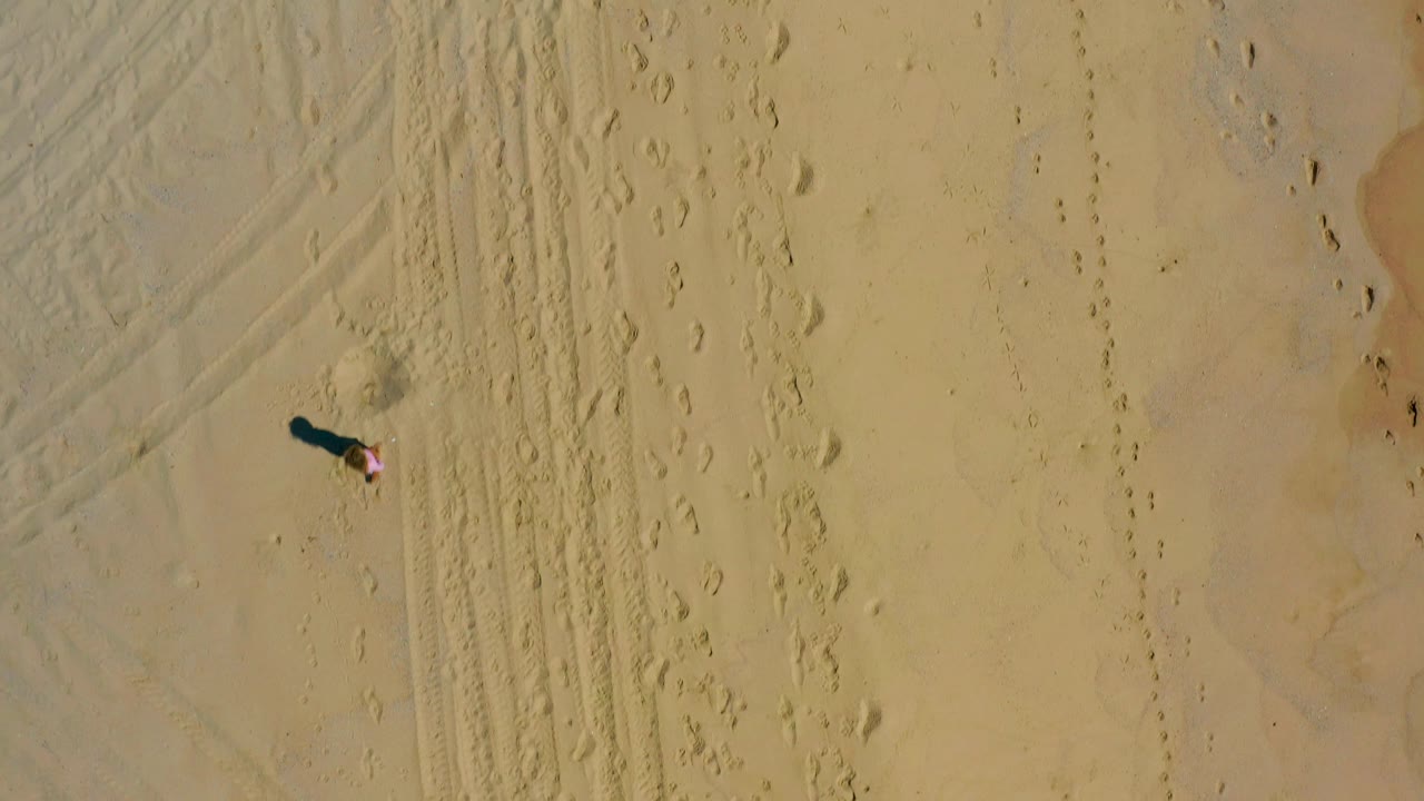 Near-straight-down view from El Cardoncito, Baja California Sur, showing the lone person and their shadow separated from dense track marks on the right side of the sandy frame.