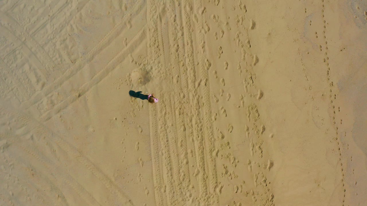 Overhead drone frame from El Cardoncito, Baja California Sur, Mexico, showing a small person near tire marks and footprints on pale sand.