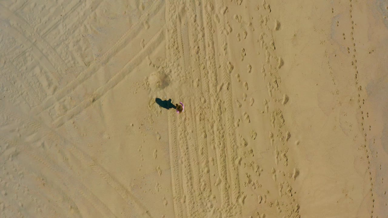 Top-down view in El Cardoncito showing the person near the upper center of the sandy frame with tire marks and footprints running vertically nearby.