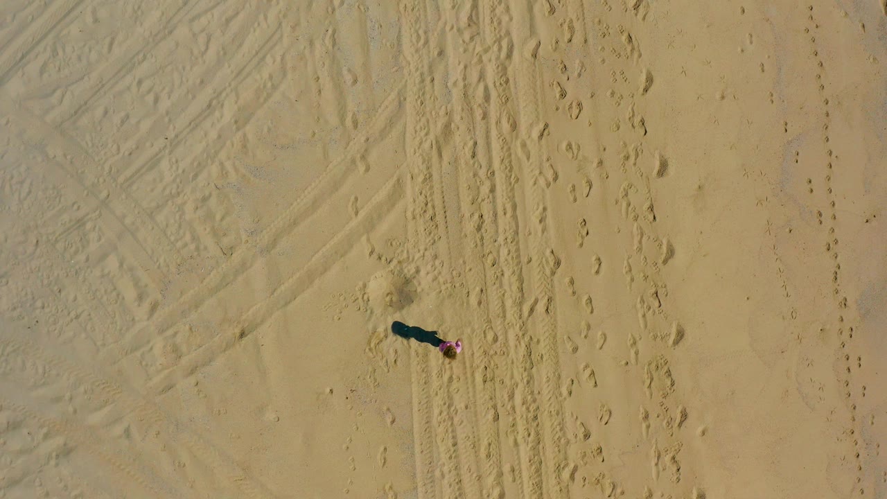 Person in pink crossing pale sand with tracks nearby.