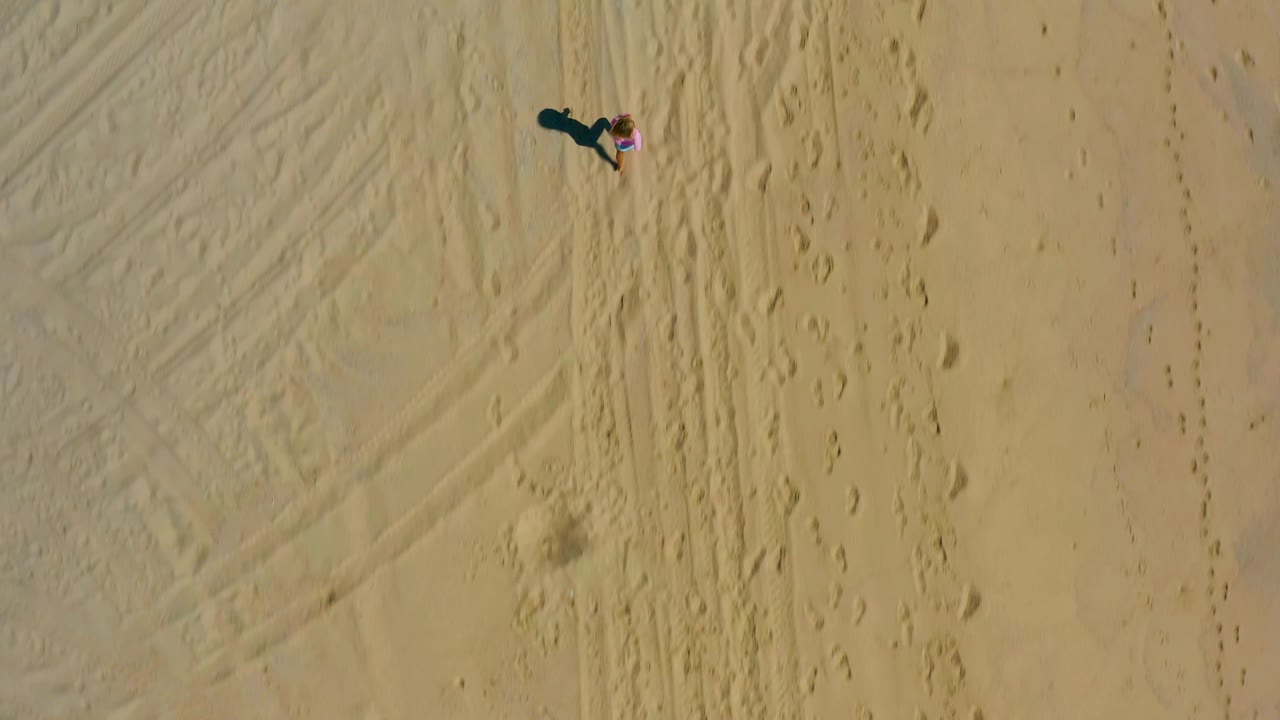 Small child on open sand seen from directly above.