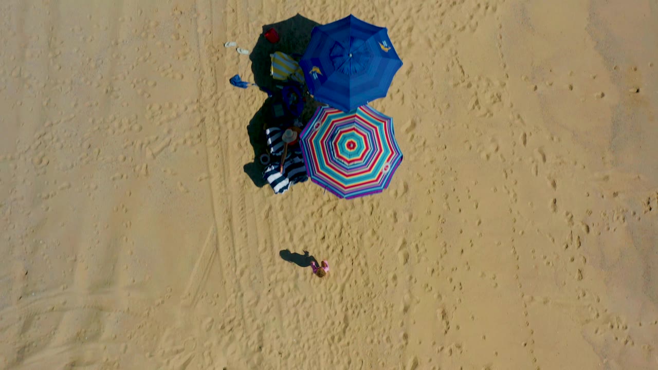Aerial view of umbrellas, beach gear, and footprints in sand.