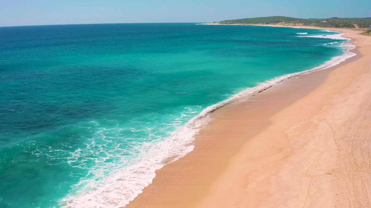 White surf rolls across shallow turquoise water toward the sand.