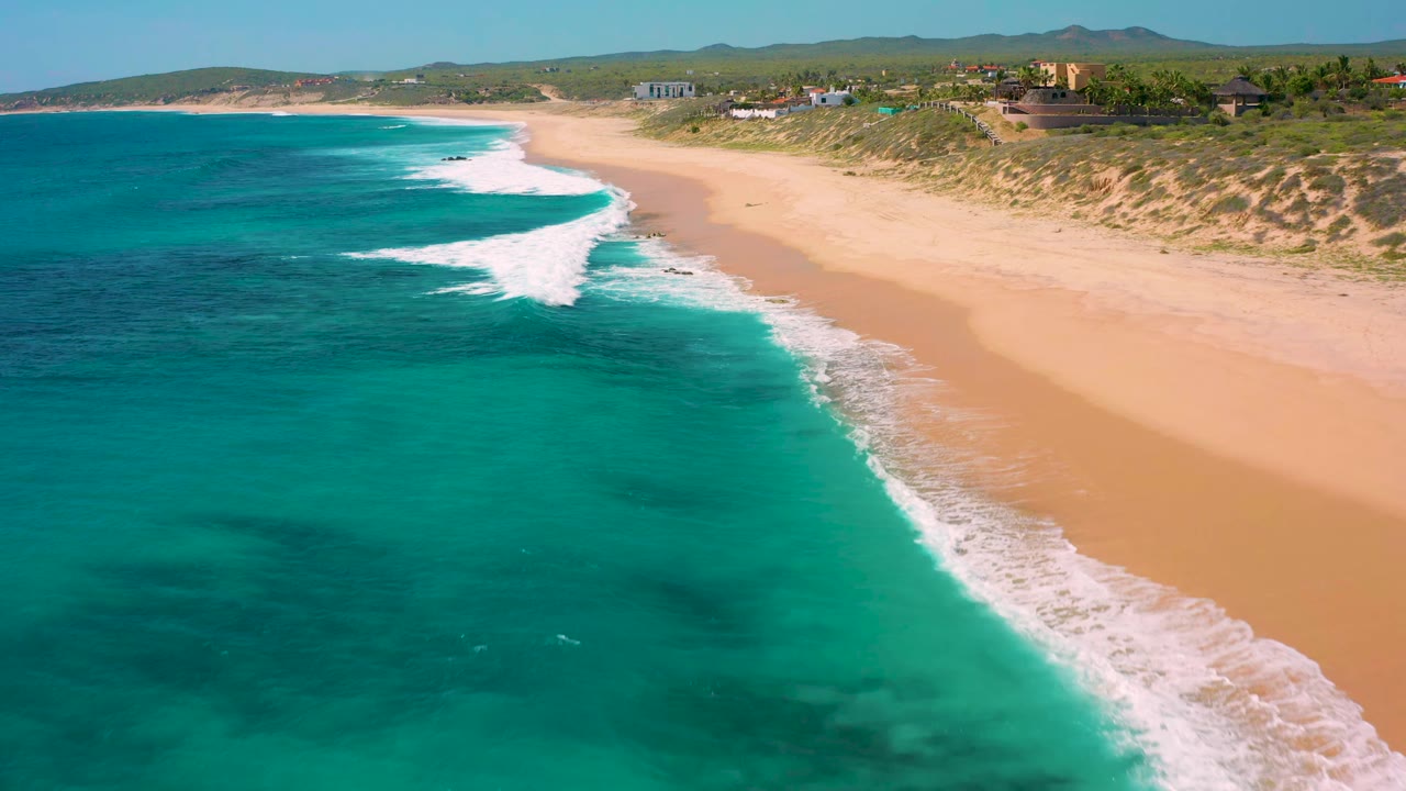 White waves run diagonally along a wide sandy shoreline