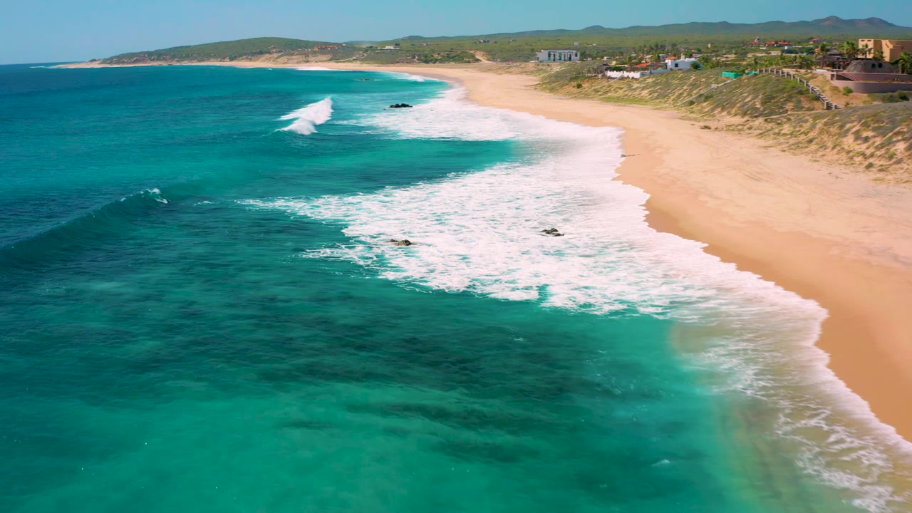Drone-style view of white waves breaking beside a long sandy shoreline