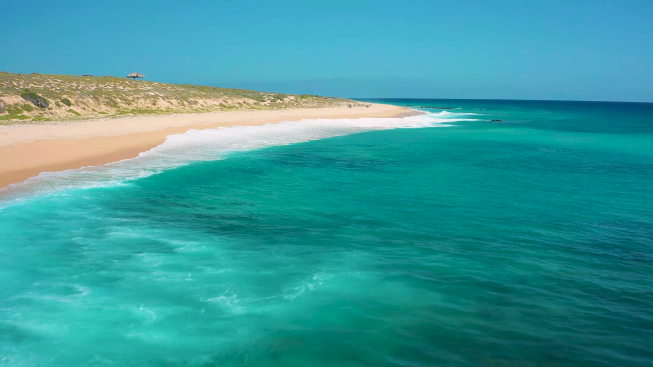 The second frame shows El Cardoncito surf tracing the edge of a pale sand beach, with deeper blue water offshore and no visible people.