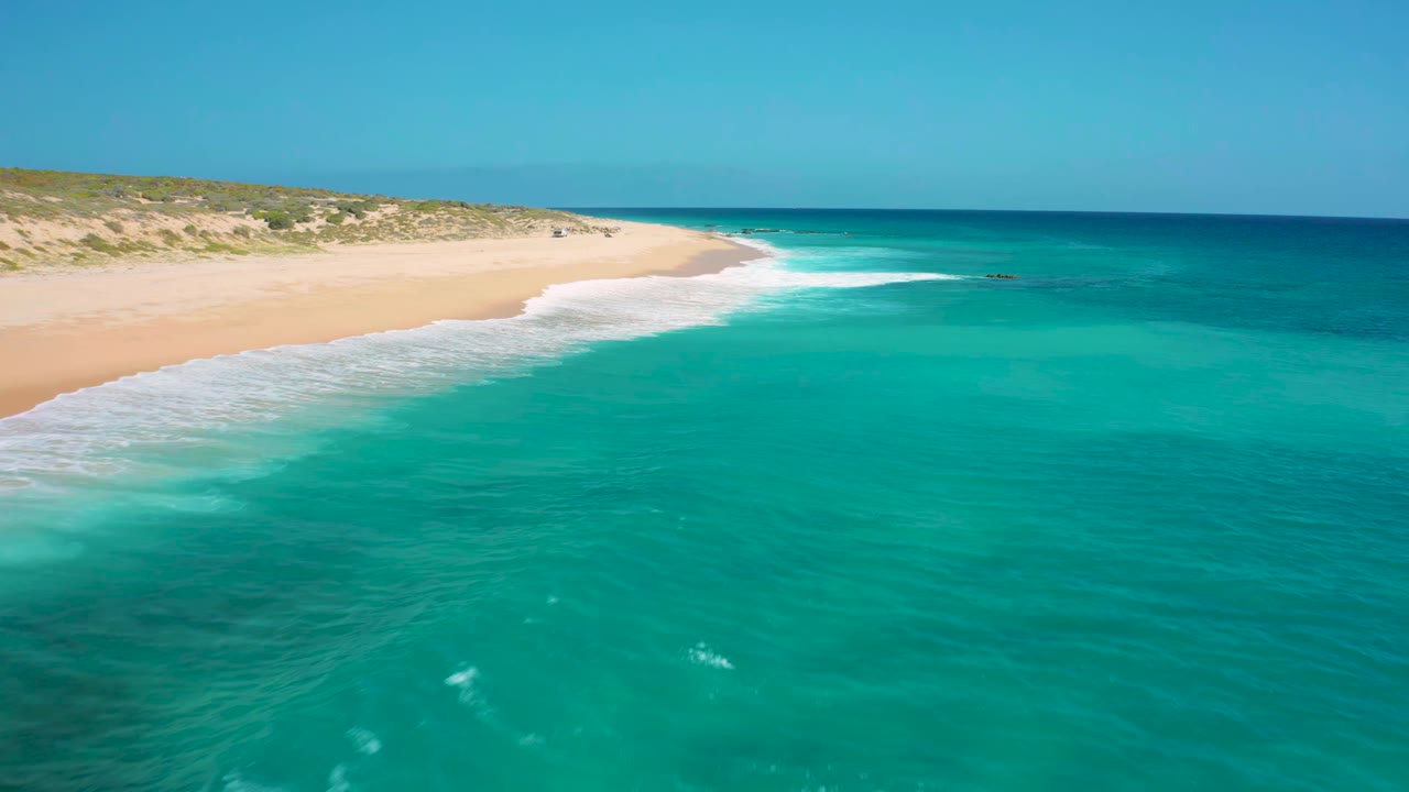 White surf breaking along a pale sand shoreline