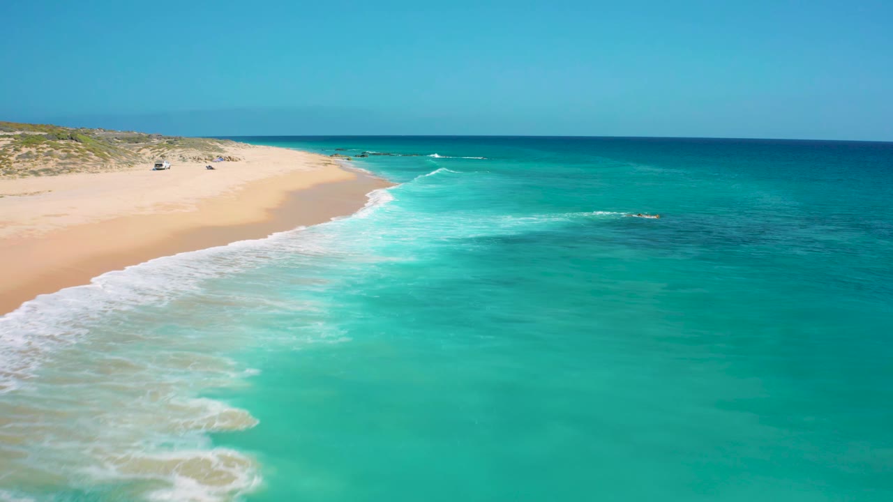 Green ocean water breaks in white foam beside a wide sand beach.