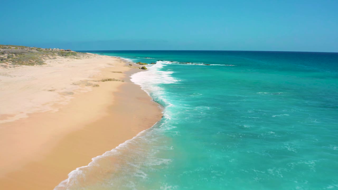 Foamy waves break along a wide sandy shoreline.