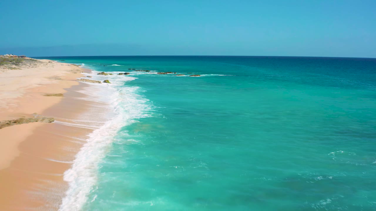 White waves curve along the sand under bright blue water.